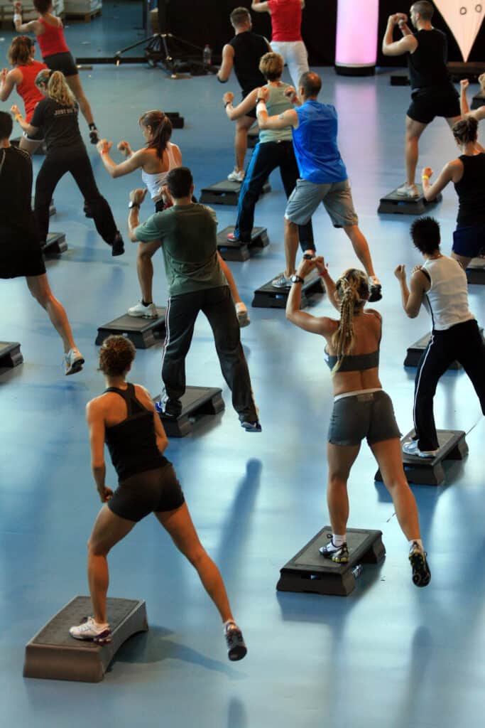 Fitness Step : Entraînement Dynamique en Groupe Cours de fitness dynamique avec un groupe de personnes en sportswear faisant du step aérobic et des mouvements de boxe sur des plateformes bleues.