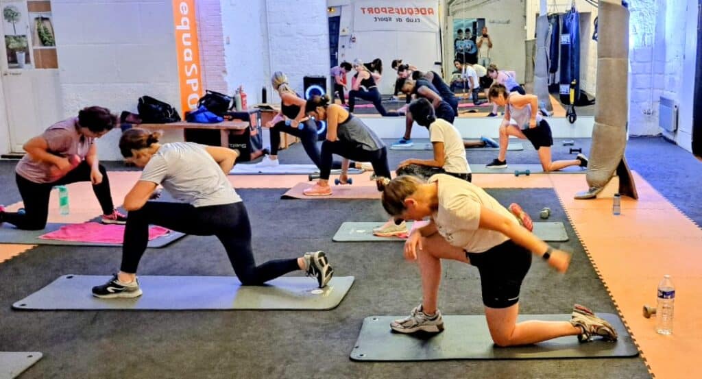Cours de Fitness Collectif Adequasport et Renforcement Séance de fitness collective chez equaSPORT avec exercices de fentes et haltères sur tapis de sport.