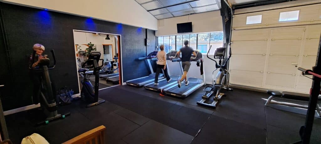 Équipements de Cardio et Tapis de Course en Salle de Sport Salle de sport moderne : personnes s'entraînant sur tapis de course et vélos elliptiques sous des lumières bleues.